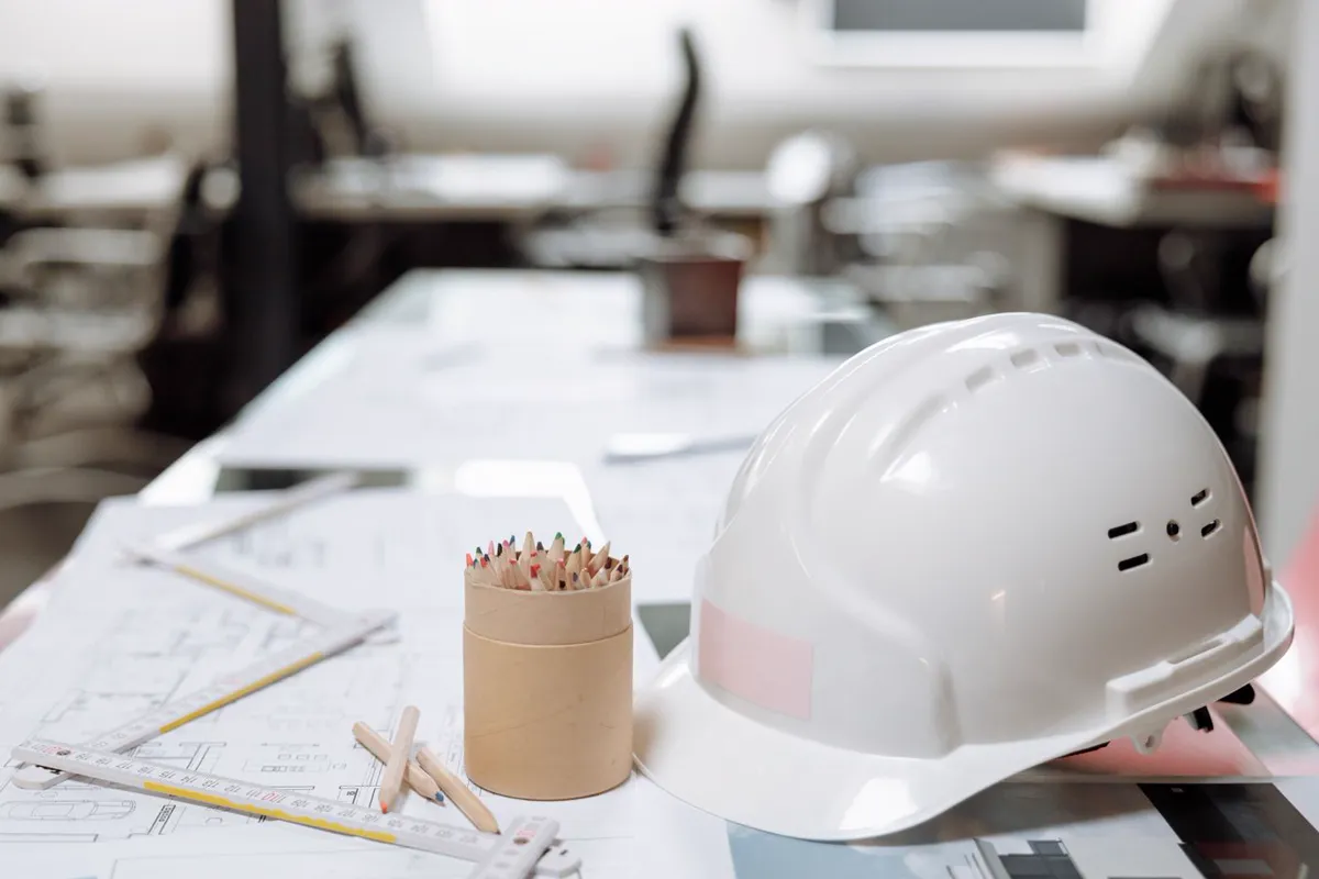 Schutzhelm und Unterlagen am Schreibtisch, Symbol für Arbeitsplatzevaluierung